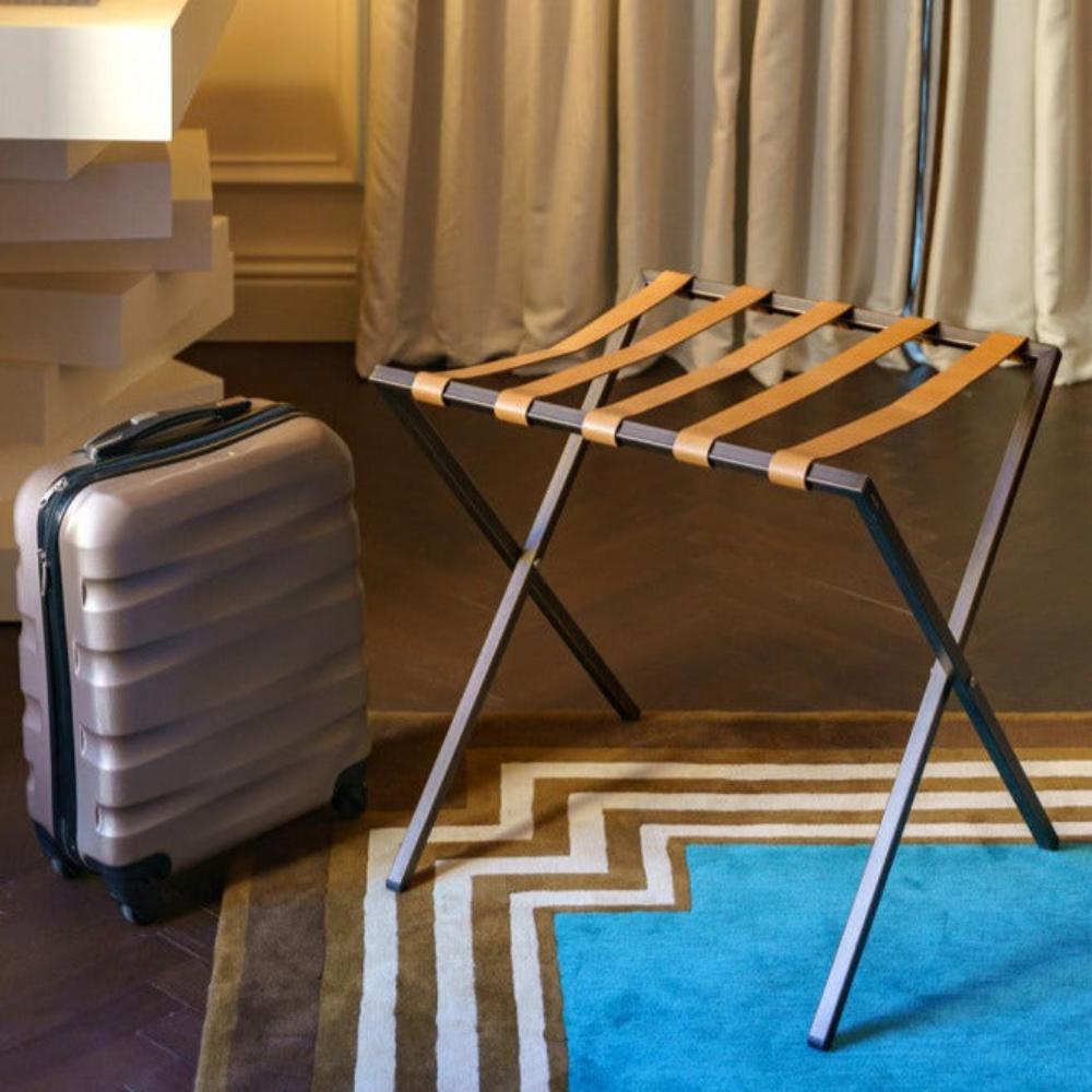 A foldable metal luggage rack with tan leather straps displayed in a luxurious setting, featuring a stylish and practical design.