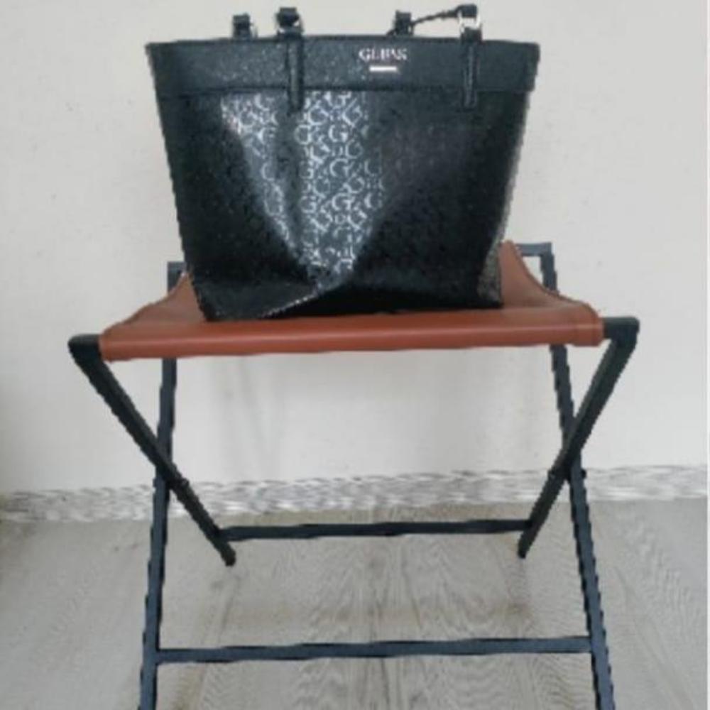 A brown leather foldable metal rack displayed against a neutral wall, holding a stylish patterned handbag, showcasing its versatility for storage