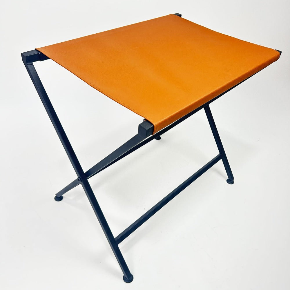 A foldable metal suitcase rack with a genuine leather top in orange, showcasing a sleek and durable design perfect for guest rooms or travel use.