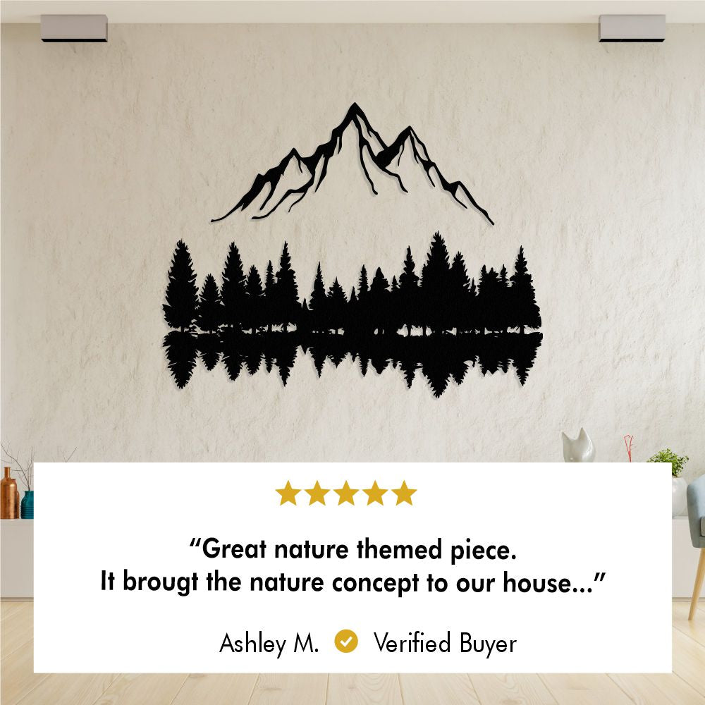 Metal wall art of a mountain and pine tree reflection displayed on a light-textured wall. Below is a 5-star review from Ashley M., a verified buyer, stating: "Great nature-themed piece. It brought the nature concept to our house."