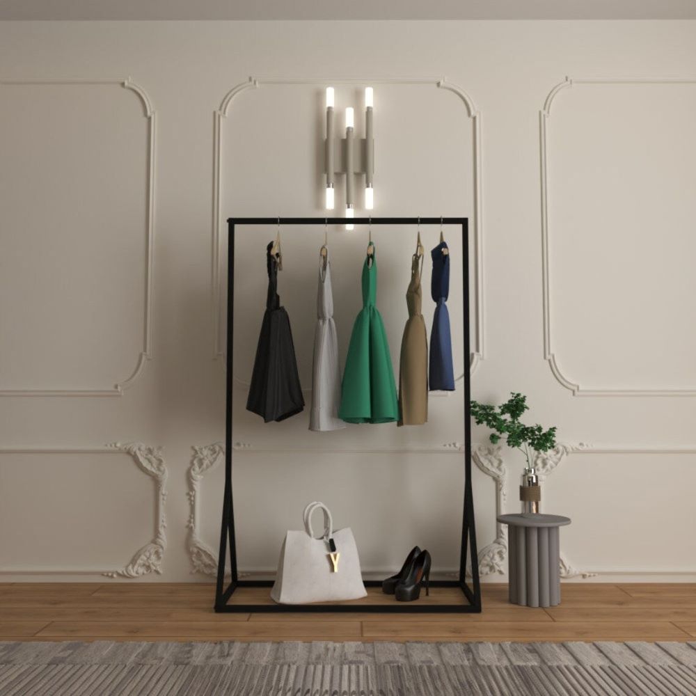 A front-facing view of a freestanding black metal clothes rail holding stylish dresses on wooden hangers, with a white bag and black heels on the bottom shelf, set in a modern room with elegant paneling and soft lighting.