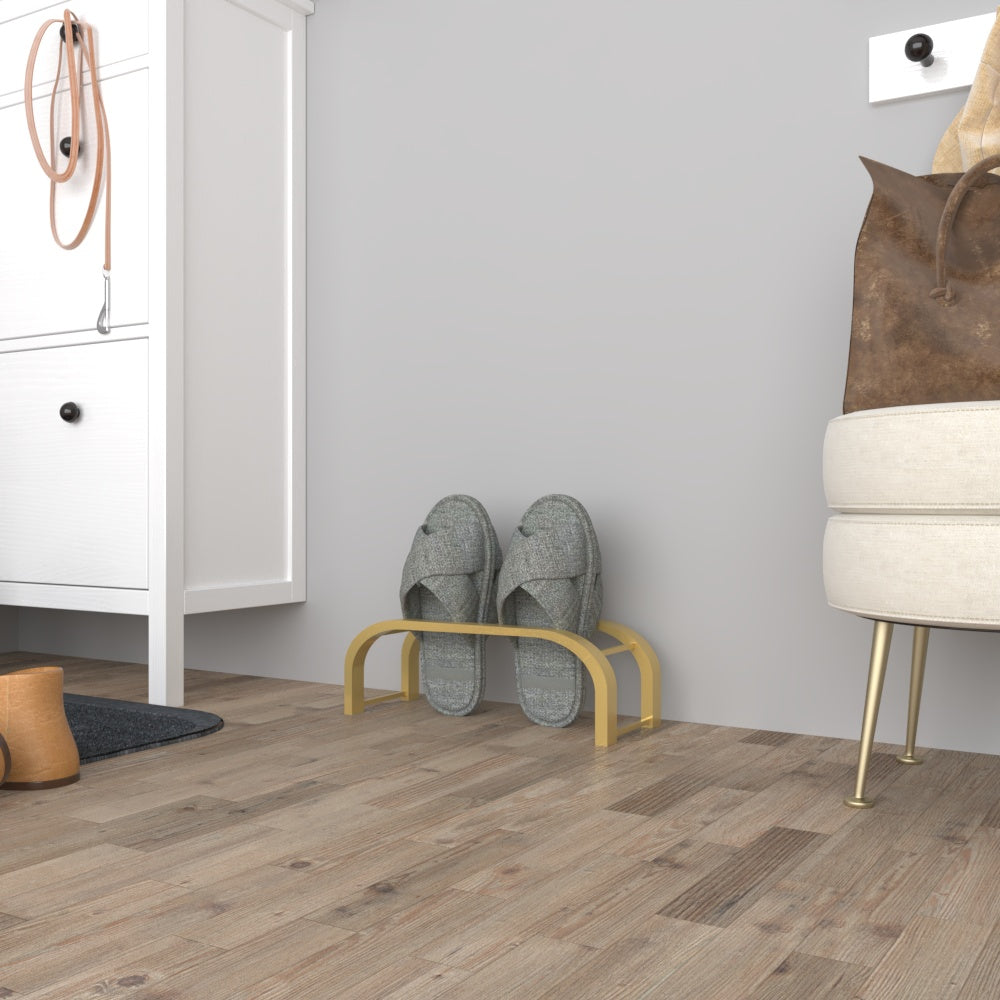 A gold minimalist slipper storage rack with gray slippers, set in a stylish entryway with wooden flooring and a beige ottoman nearby