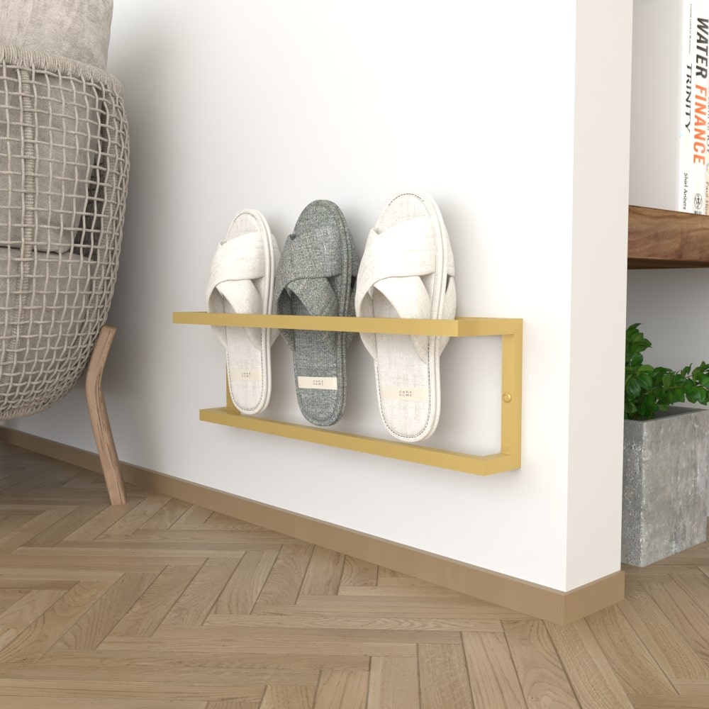 A sleek wall-mounted slipper rack in gold, holding three pairs of slippers against a light wall, with wooden flooring and a nearby bookshelf adding warmth to the space.