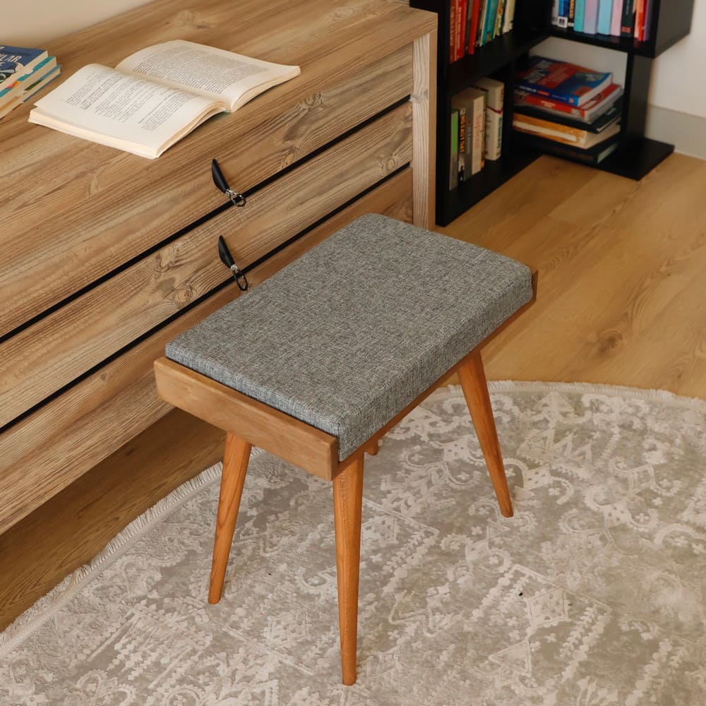 Grey cushioned bench with wooden legs, photographed close up in front of a wooden storage unit.