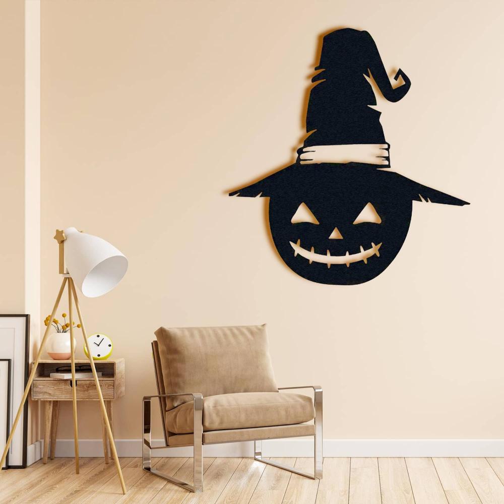 Jack-o'-lantern-shaped metal wall decor with a witch's hat, mounted above a beige armchair in a cozy living space with a floor lamp nearby.