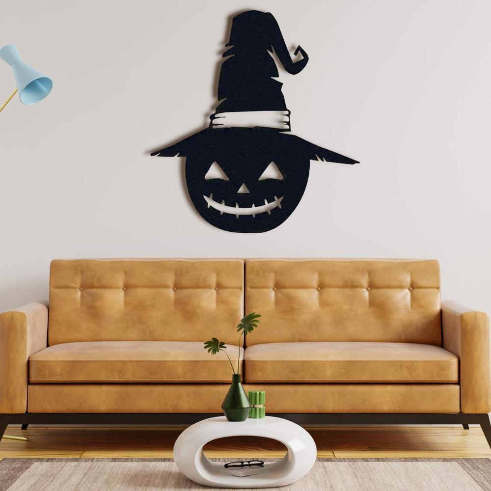 Black metal Halloween wall decor featuring a grinning jack-o'-lantern wearing a witch's hat, mounted above a tan leather sofa with a modern coffee table in front.