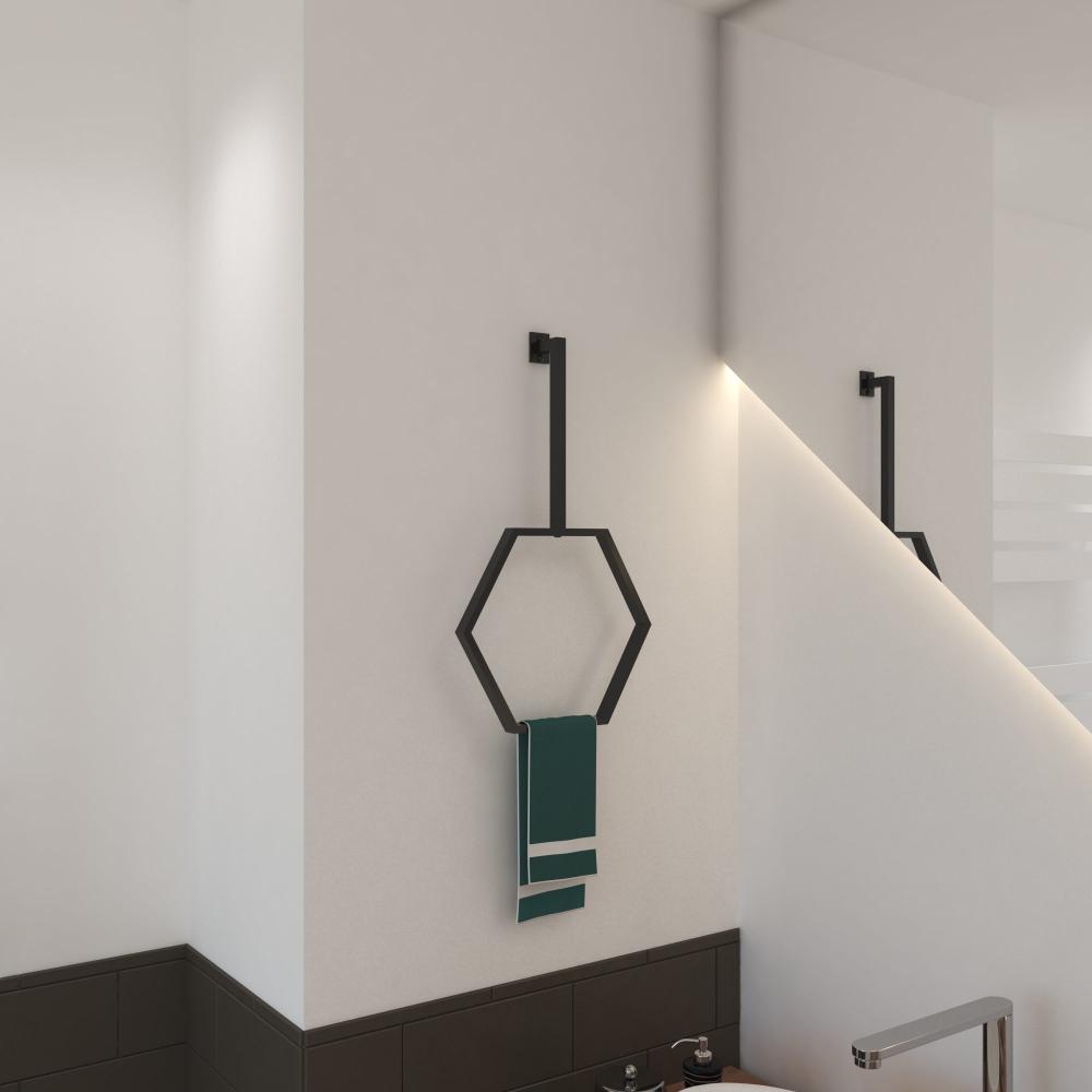 A modern hexagonal towel ring in a matte black finish, wall-mounted on a white bathroom wall with a green towel hanging neatly, showcasing minimalist design.