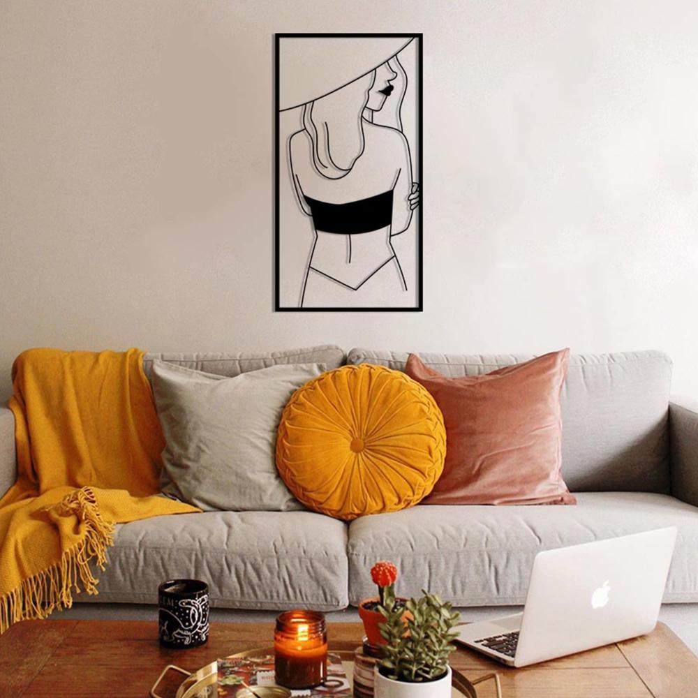 Modern living room featuring a metal wall art of a woman wearing a hat and facing sideways, mounted above a cozy gray sofa with colorful cushions and a blanket.