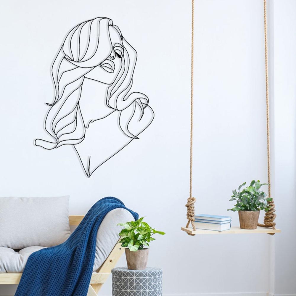 Minimalist line art metal wall decor of a woman with long, wavy hair, installed on a white wall. The scene includes a cozy setup with a light wood bench adorned with a gray cushion and a blue blanket, a patterned round stool, and a hanging wooden swing shelf with potted plants and books.