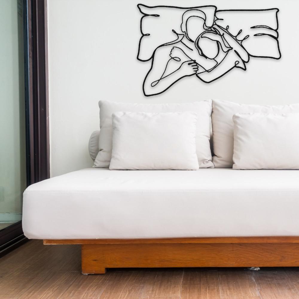 Black abstract metal wall art featuring a couple embracing, displayed above a minimalist white sofa with wooden accents.