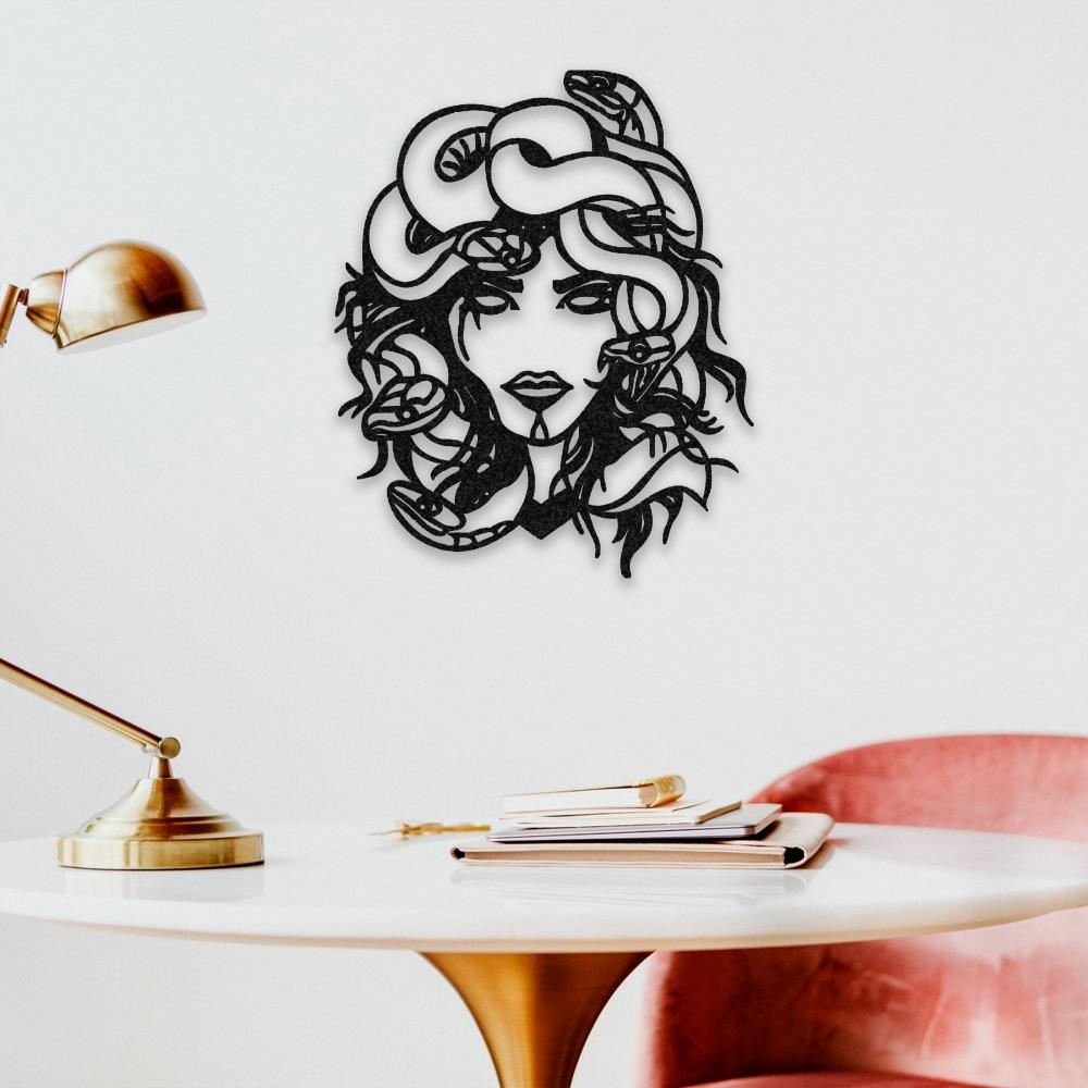 Elegant Medusa metal wall art featuring intricate snake details in her hair, mounted on a white wall above a modern white table with a gold lamp and a pink velvet chair.