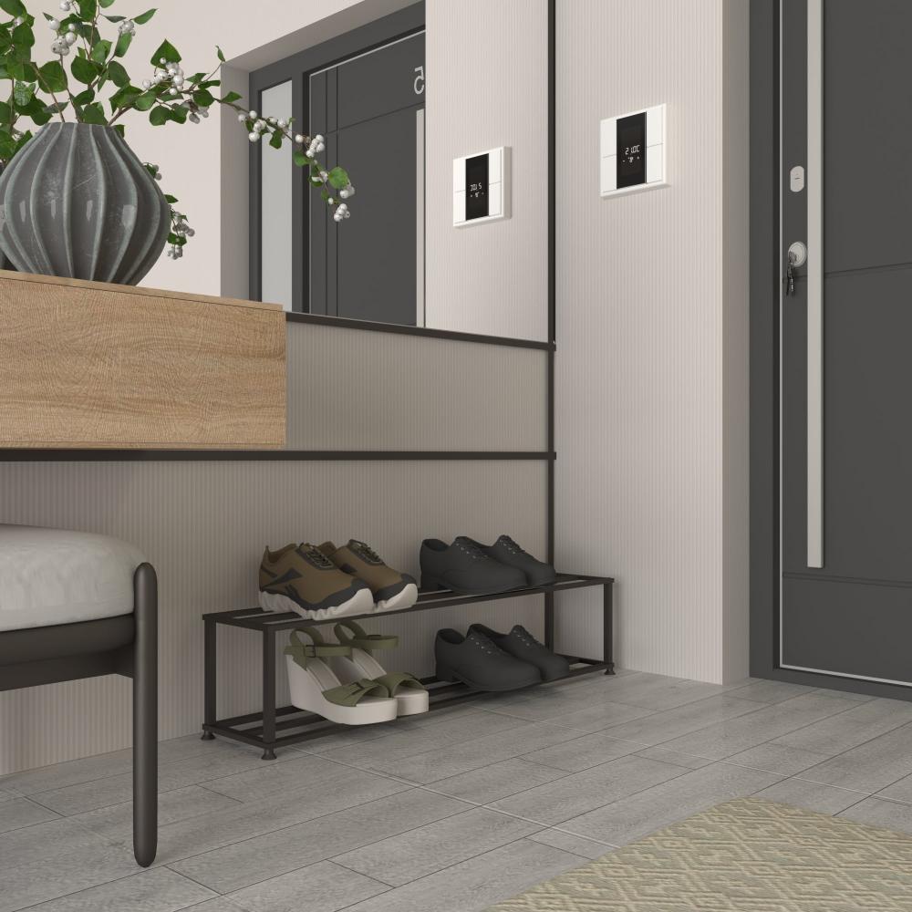  A minimalist black metal shoe rack positioned in a sleek, modern entryway. The rack features two tiers, holding various shoes, including black formal shoes and casual sneakers. The stylish space includes a wooden bench with a green plant in a vase, a dark door with a digital lock, and a mirror reflecting the contemporary design. The light-colored walls and flooring create a clean and welcoming atmosphere, highlighting the functional elegance of the shoe rack.