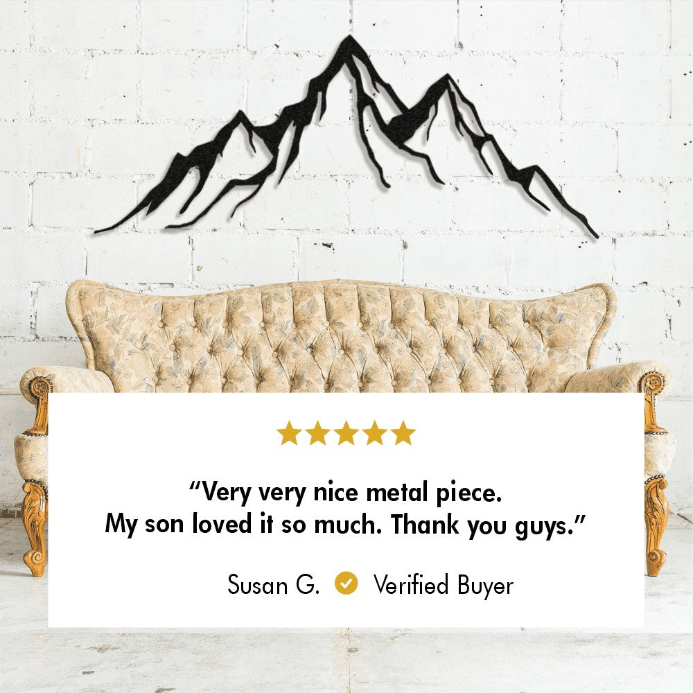 Metal mountain wall decor displayed above a vintage-style beige couch, accompanied by a five-star review from Susan G., a verified buyer, stating, "Very very nice metal piece. My son loved it so much. Thank you guys."