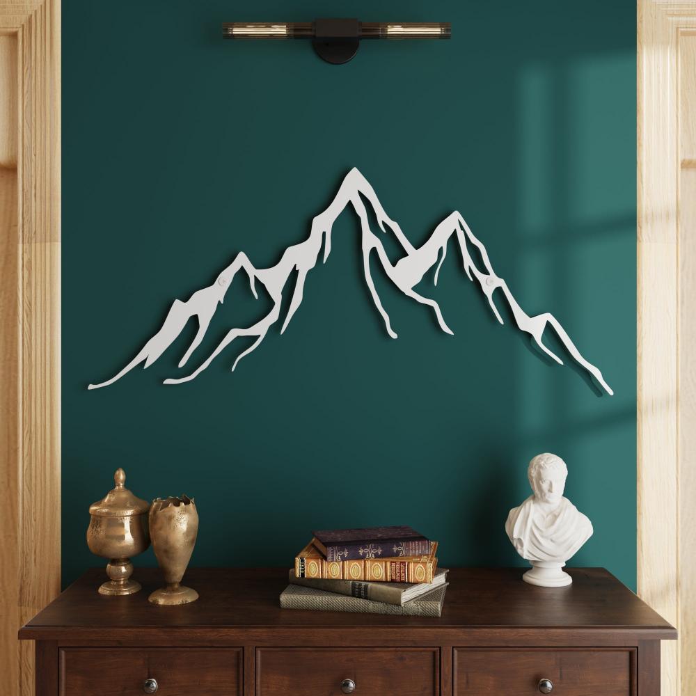 A cozy living space features a minimalist white metal mountain wall art on a deep green accent wall. Below, a dark wooden sideboard is adorned with decorative items including a brass urn, a stack of antique books, and a classical bust sculpture, creating a sophisticated and serene atmosphere.