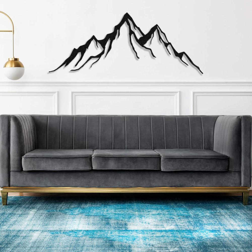 Metal mountain wall decor displayed above a modern gray sofa in a stylish living room with a blue-toned rug and white paneling, creating a sleek and contemporary aesthetic.