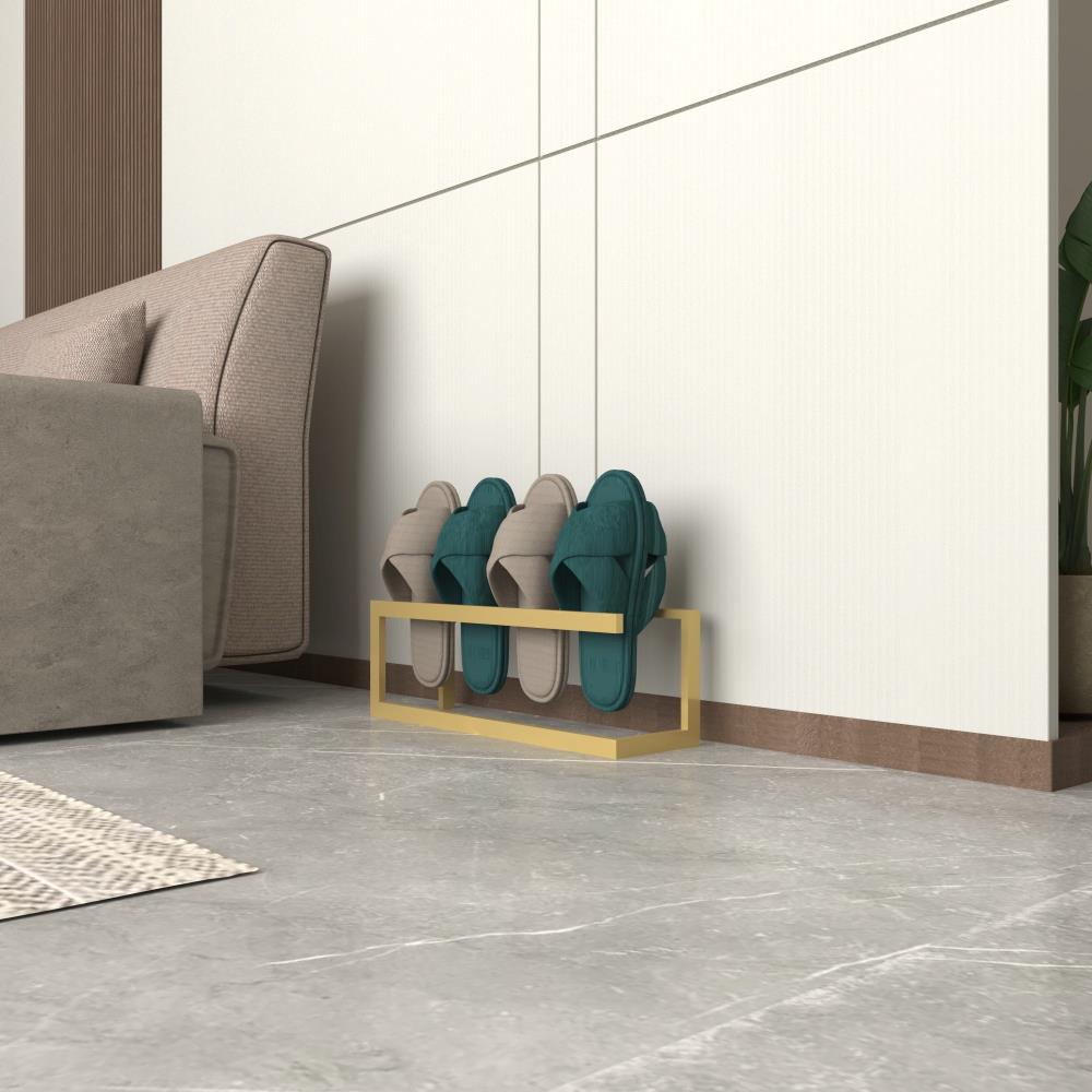 A gold metal slipper rack holding three pairs of slippers, placed in a bright and contemporary living space