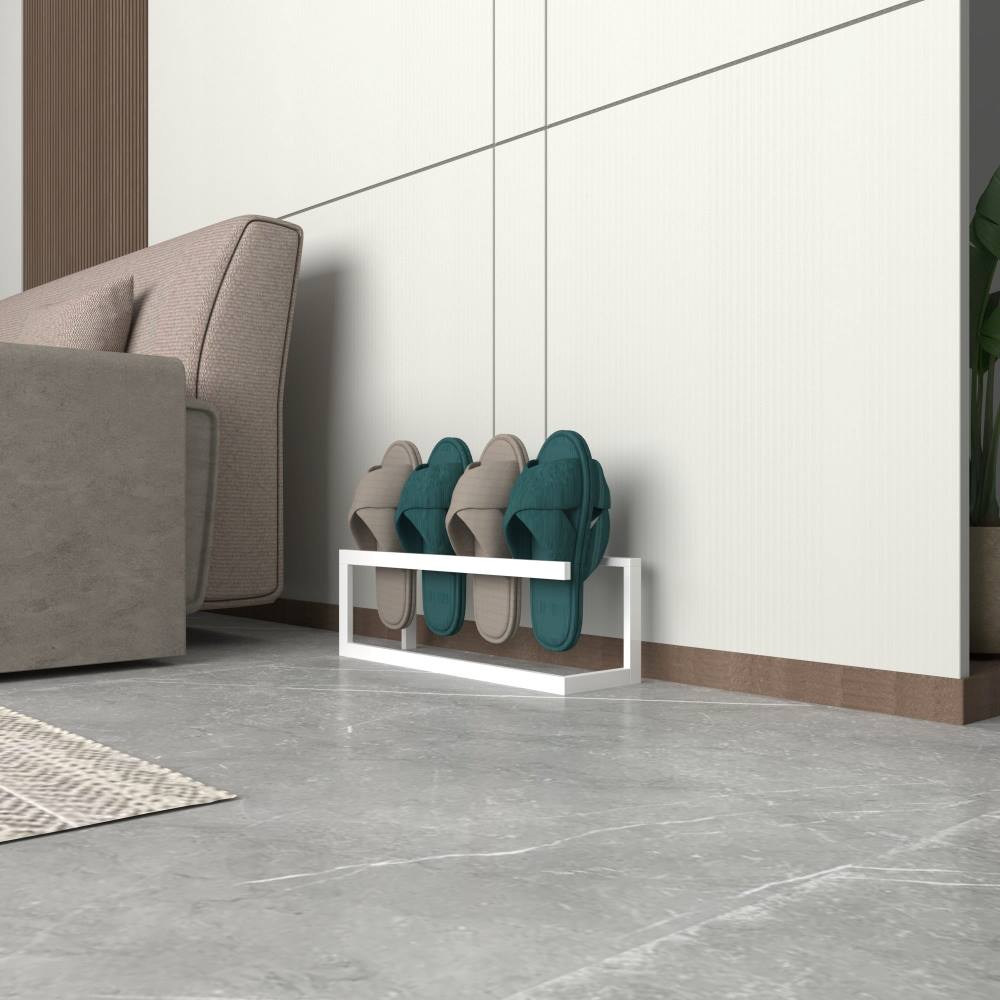 A white metal slipper rack holding three pairs of slippers, placed near a modern armchair on a polished tiled floor