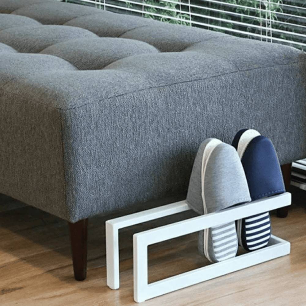 A white slipper rack placed under a bench, neatly holding two pairs of slippers with a minimalist design