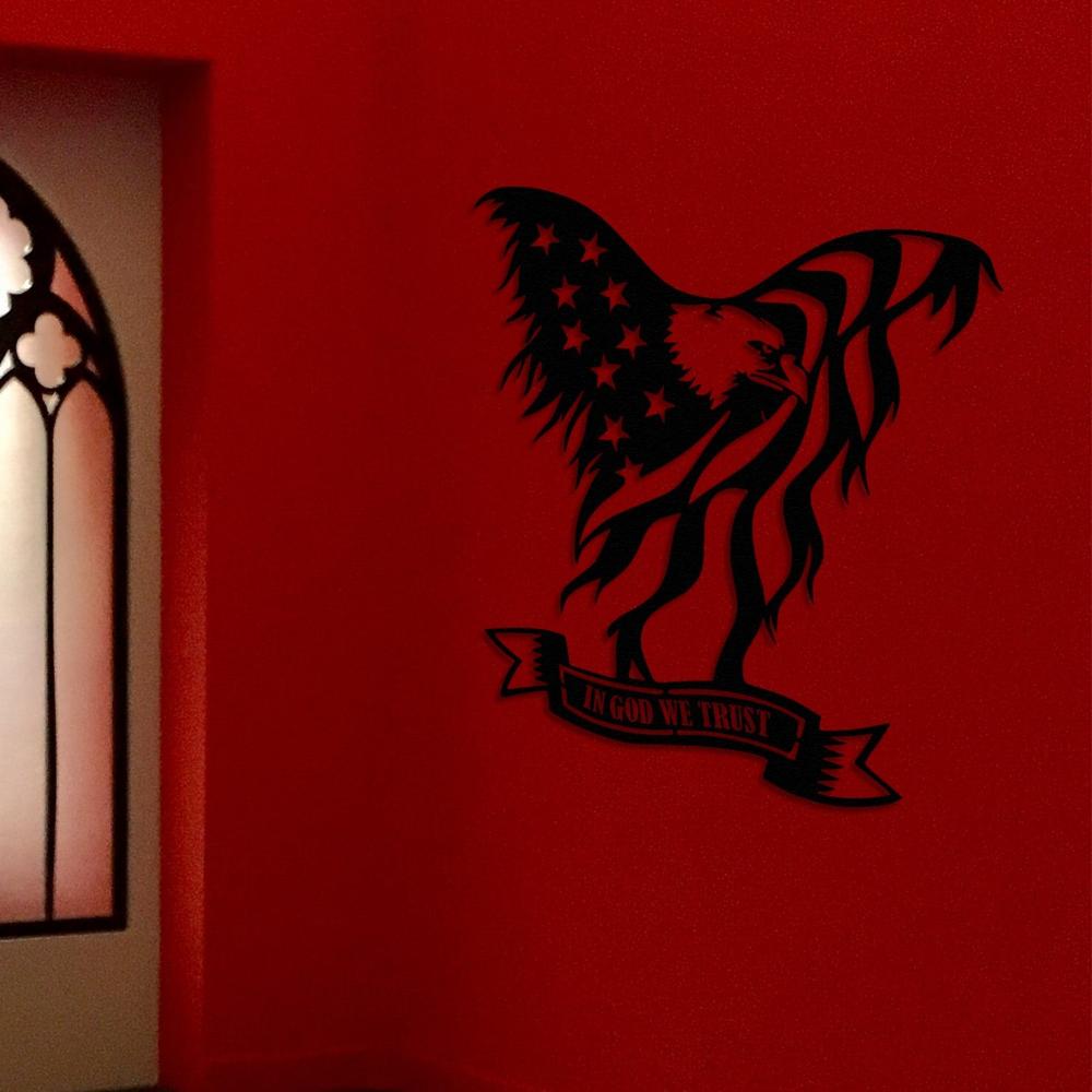 Black metal wall art of an American bald eagle with the U.S. flag and "In God We Trust" text, displayed on a red wall near a stained-glass window with a gothic arch design.