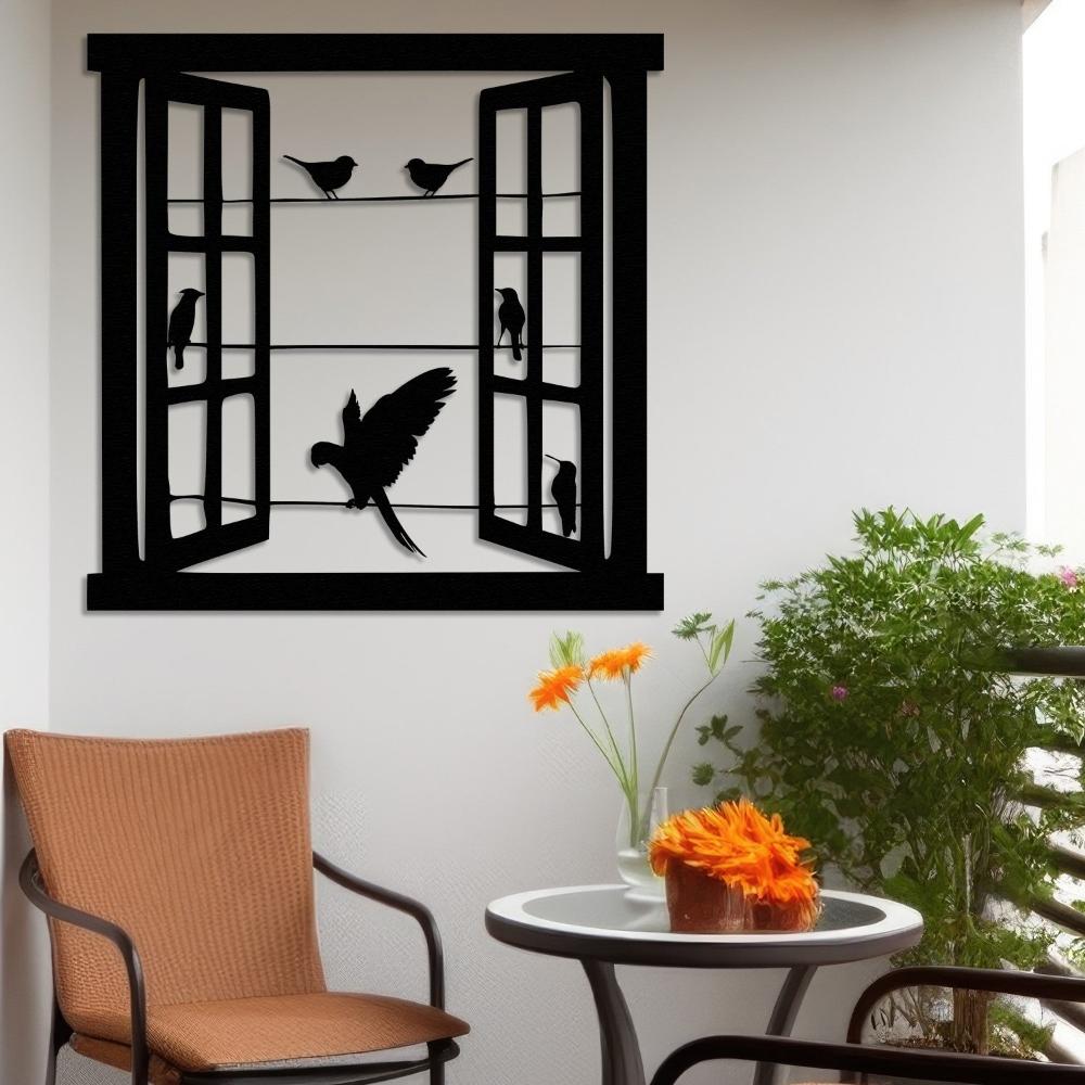 Metal wall art depicting an open window with birds perched on wires and one bird in mid-flight, displayed in a cozy balcony setting with a round table, chair, and vibrant flowers.