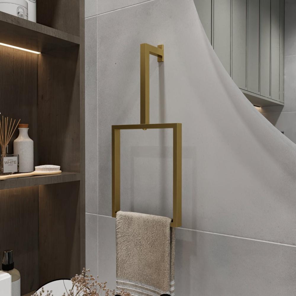 A minimalist gold-finished vertical towel ring is mounted on a light gray wall. The elegant rectangular design holds a beige towel, adding a luxurious touch to the bathroom decor. The sleek and modern towel ring enhances the sophisticated and clean ambiance of the space, perfectly complementing the surrounding minimalist design elements.