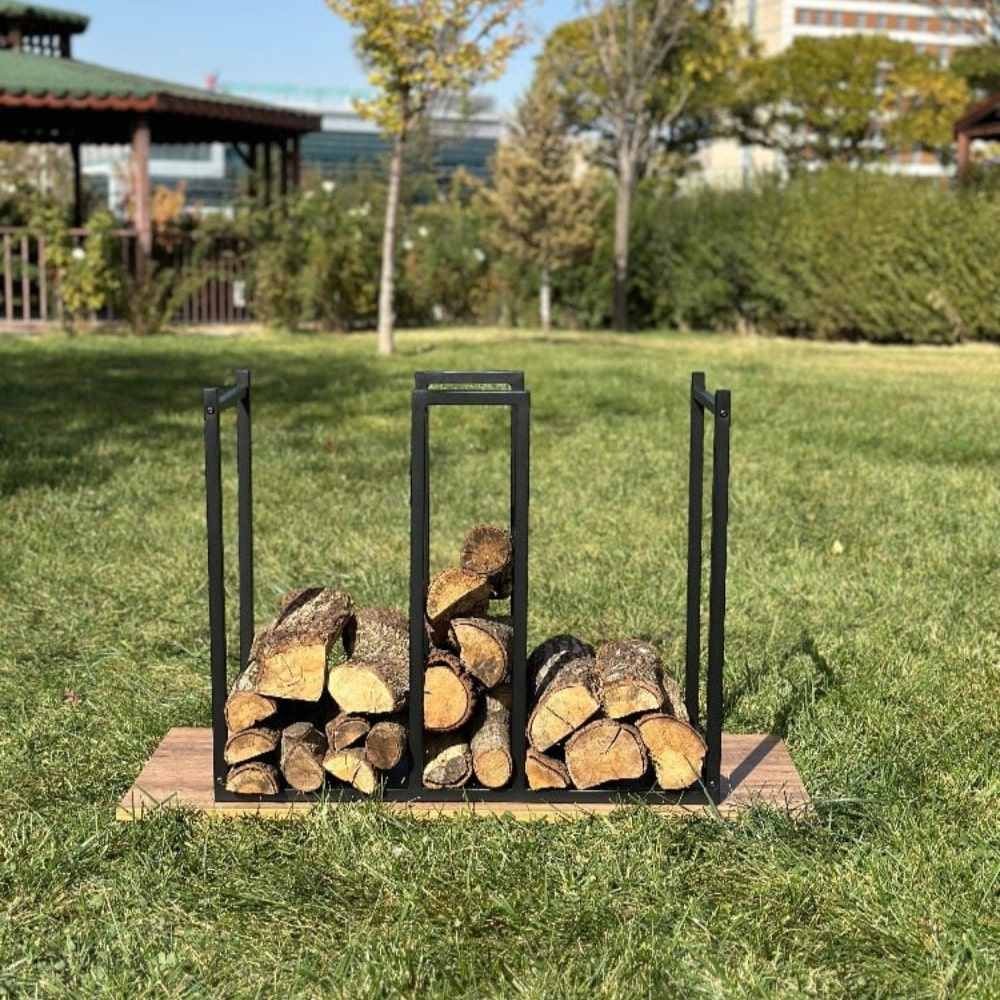 A sleek black metal log holder with an integrated kindling section, placed outdoors on grass, holding neatly arranged firewood