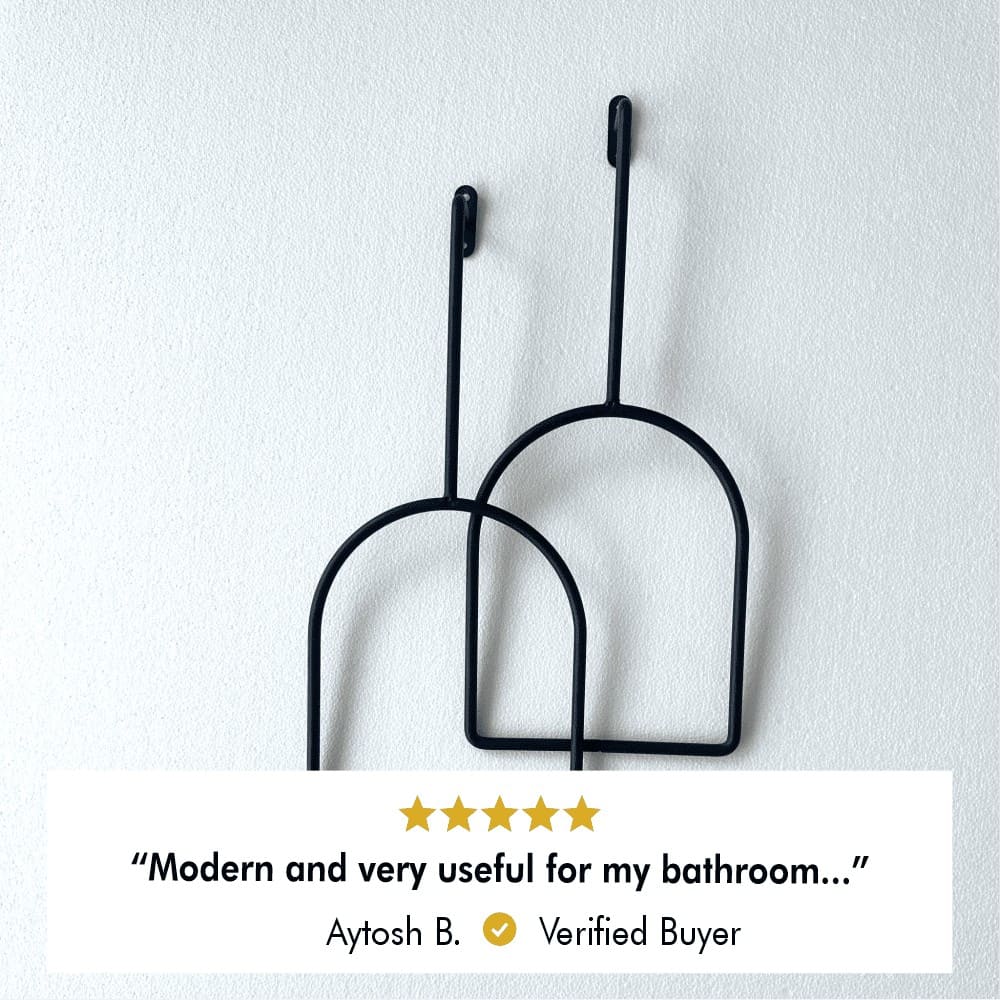 Pair of minimalist black wall hooks placed on a wooden surface, showcasing a three-dimensional design, with review from verified buyer, Aytosh B., stating" Modern and very useful for my bathroom"