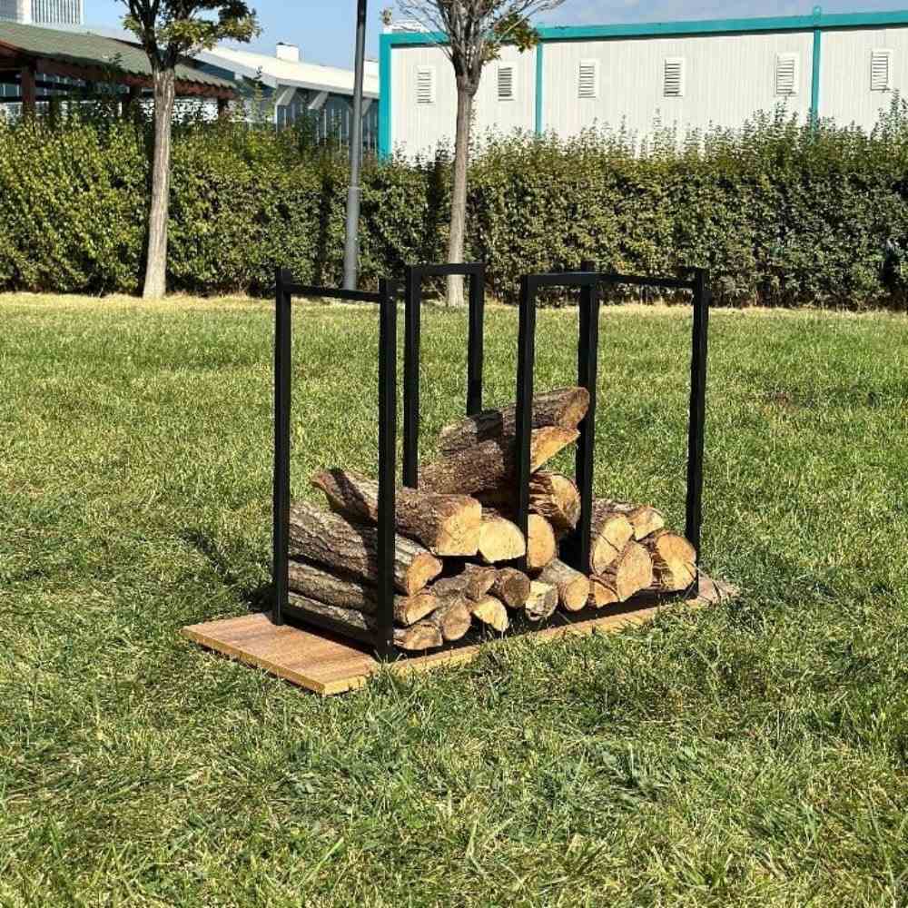 A black metal log holder with kindling storage, standing on a wooden base outdoors, holding chopped logs and kindling