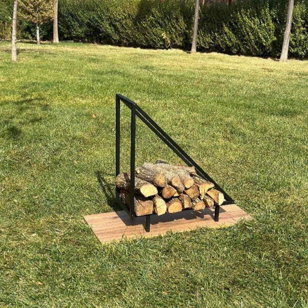 A black metal wood rack with a triangular design placed outdoors on a wooden base, holding logs of firewood, blending with the natural grassy background.