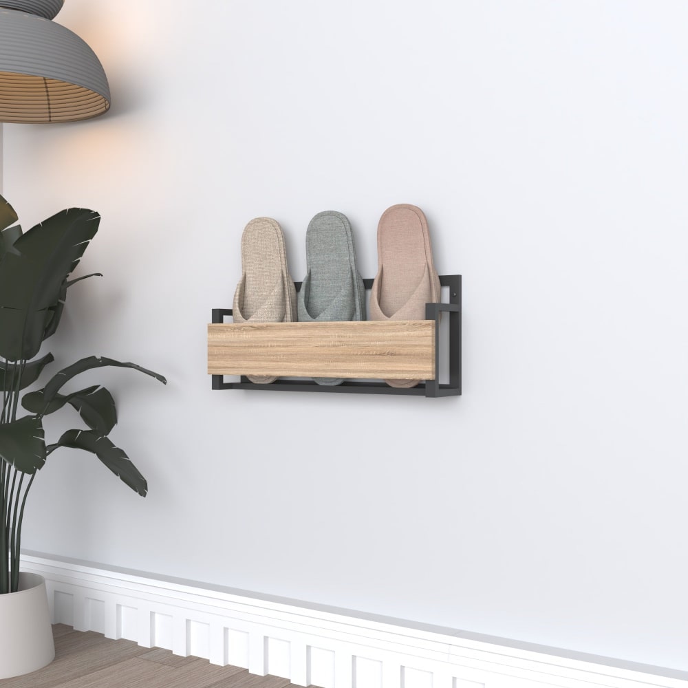 A modern wall-mounted slipper rack with a sleek black metal frame and a wooden front, holding three pairs of pastel-colored slippers, placed in a minimalist room with potted plants and wall decor