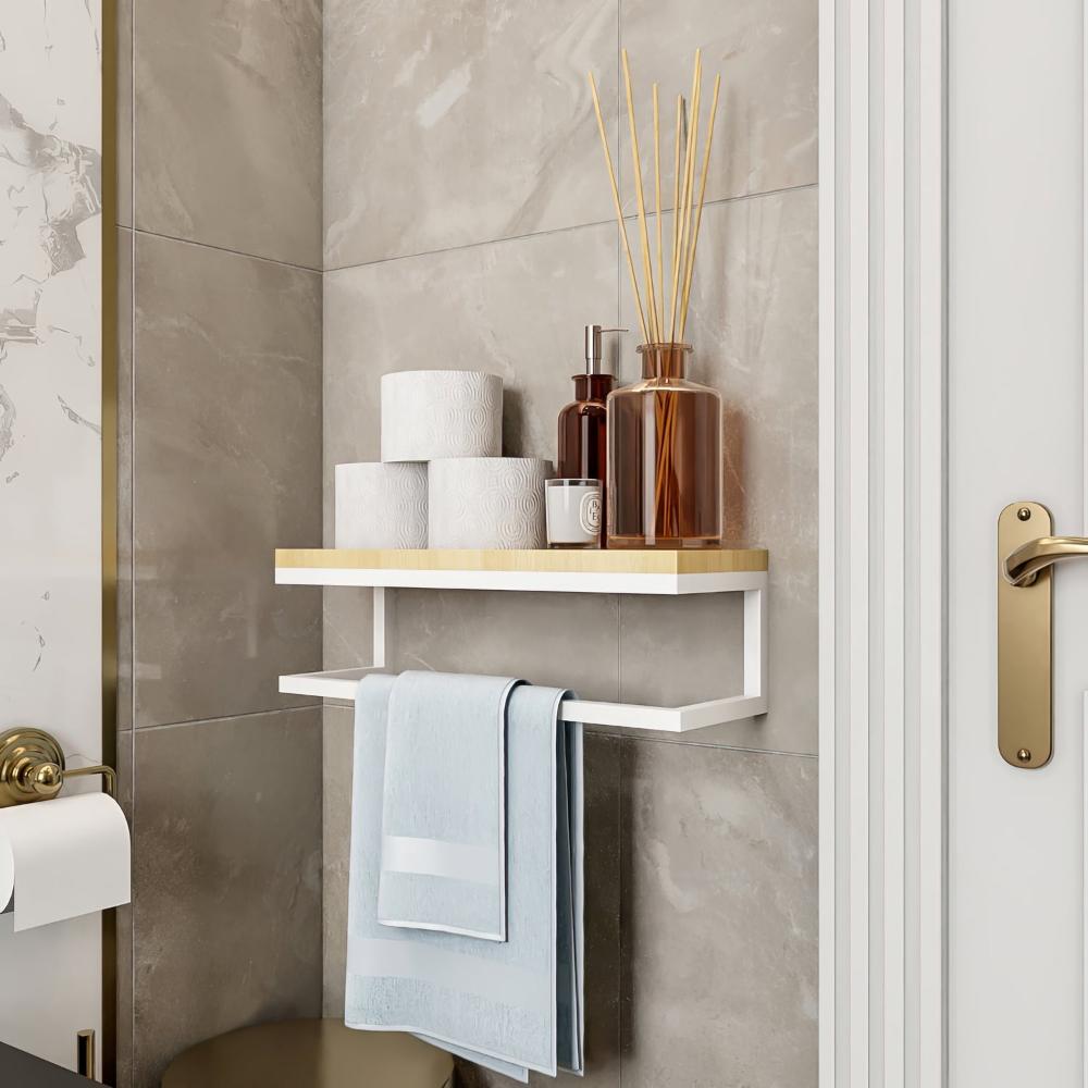 A sleek wall-mounted towel holder with a white metal frame and natural wooden shelf, placed in a bathroom corner. The shelf holds decorative jars, and a light blue towel hangs below.