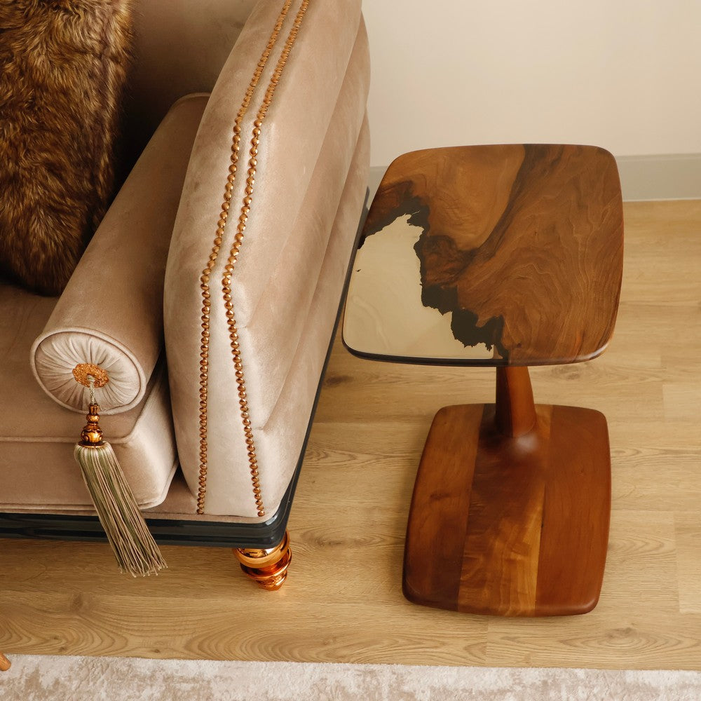 A modern wooden side table with a black resin top featuring natural wood grain patterns, positioned next to a beige sofa with gold tassel details.