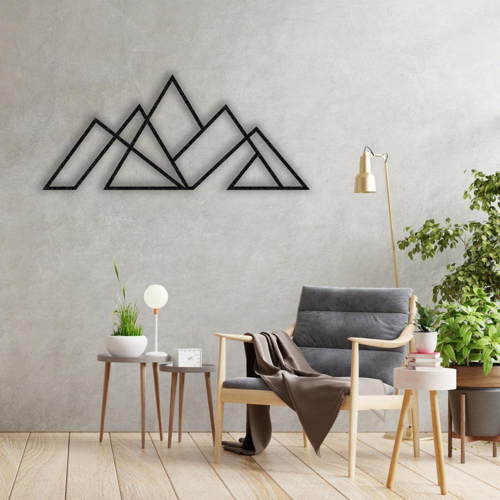 Black geometric mountain metal wall art displayed on a textured concrete wall, styled with a cozy gray armchair, light wood side tables, and green indoor plants.