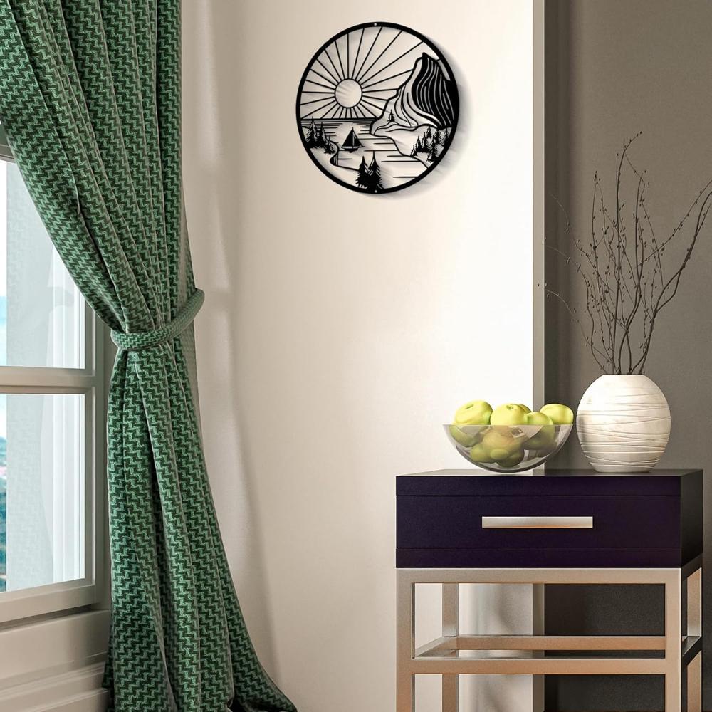 Round metal wall art showcasing a serene mountain scene with a radiant sun, trees, and a sailboat, elegantly displayed on a neutral-colored wall next to a green curtain and a modern console table with a fruit bowl and decorative vase.