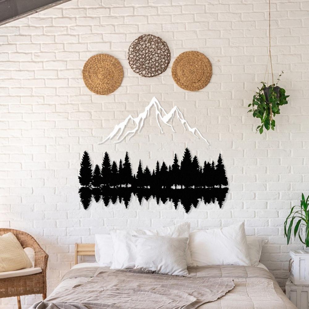 Nature-inspired metal wall art featuring mountain peaks and tree silhouettes, mounted on a white brick wall above a cozy bed adorned with neutral-tone pillows and a beige throw blanket. Decorative woven accents and a hanging plant add warmth to the serene setting.