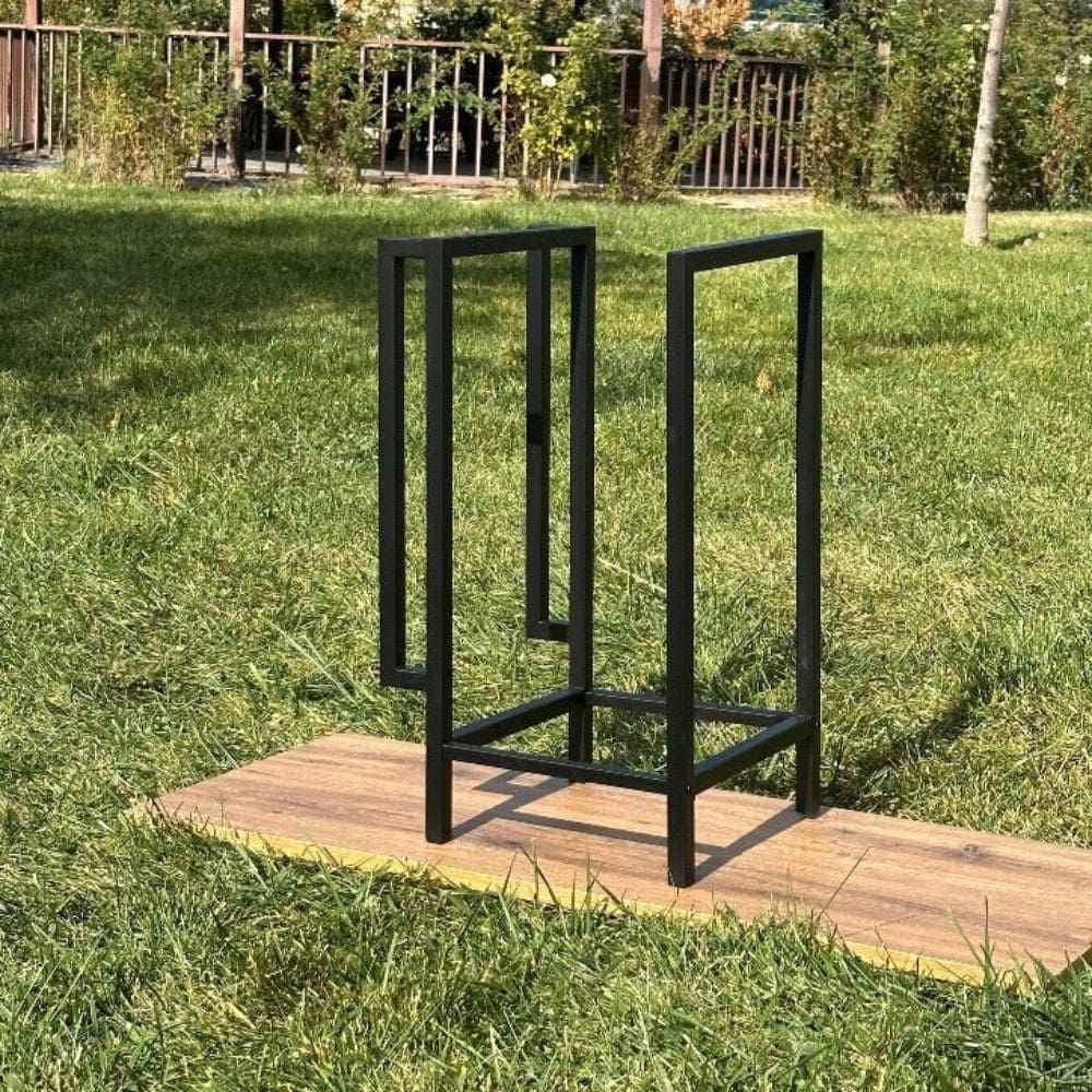 Empty black metal firewood holder displayed outdoors on a wooden plank with a green lawn backdrop