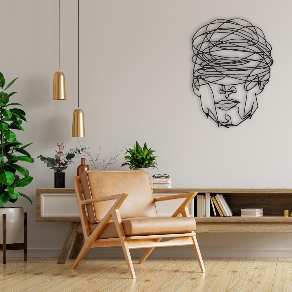 Modern living room featuring the "Overthinking Man" abstract geometric face metal wall decor mounted on a neutral wall above a wooden console, complemented by a tan leather accent chair, green plants, and gold pendant lights.