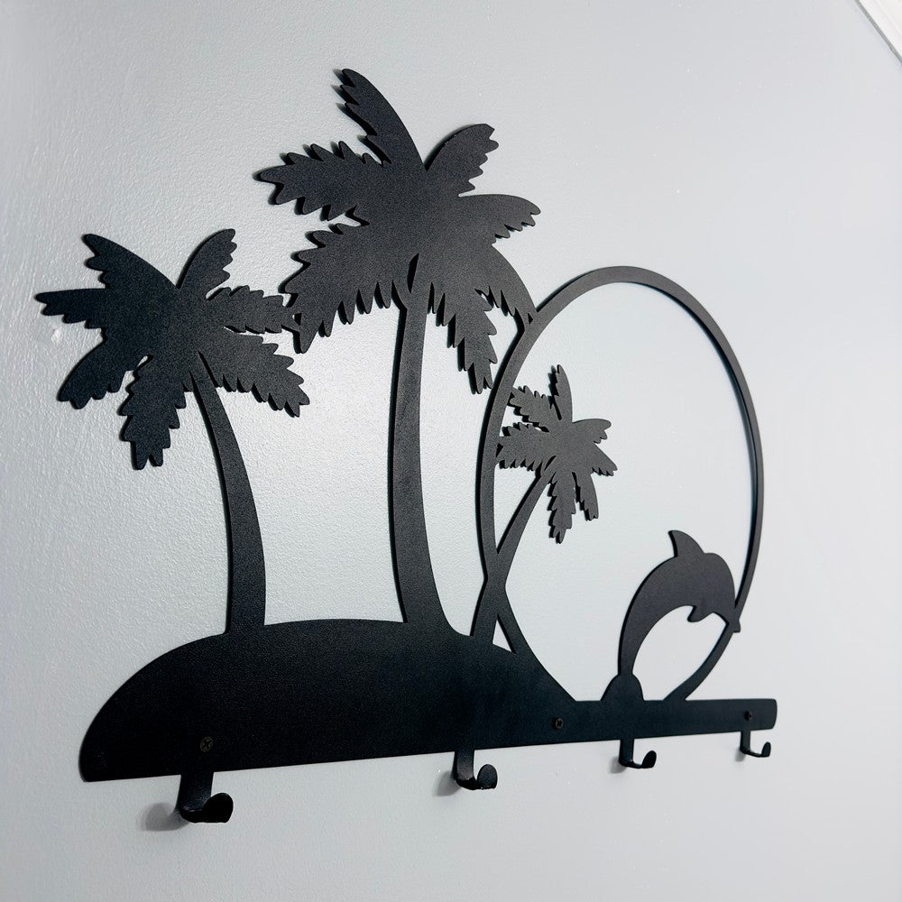 A close-up view of a black metal wall-mounted rack featuring palm trees and a dolphin jumping through a circle. The tropical design includes hooks for hanging items, blending both functionality and decorative appeal.