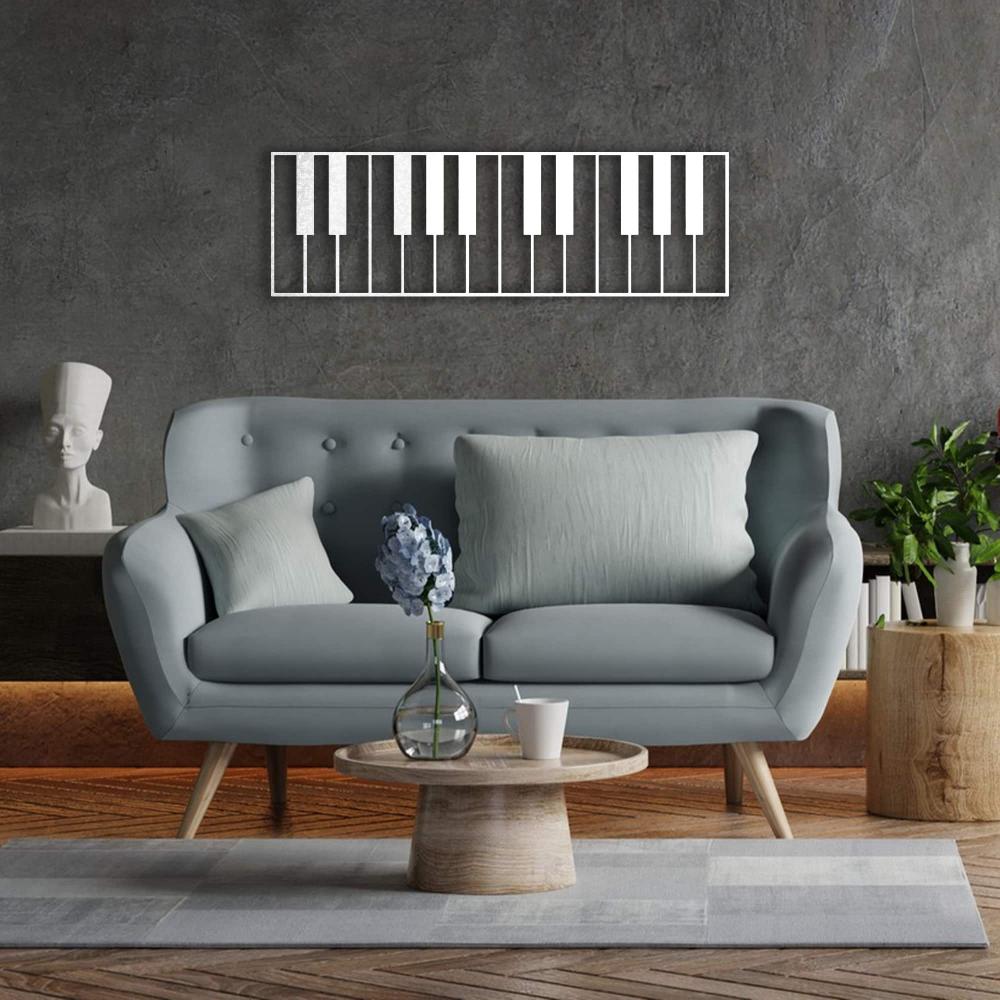 Piano keys-themed metal wall art in a sleek white design, mounted on a textured gray wall above a modern blue tufted sofa. The living space is complemented by wooden flooring, a round wooden coffee table with a flower vase, and minimalistic decor elements.