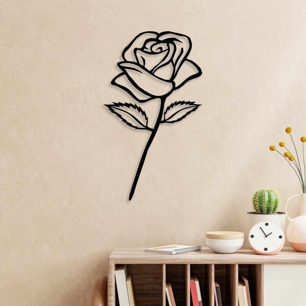 Black rose metal wall art mounted on a light beige textured wall above a wooden shelf containing books, a cactus plant, a vase with yellow flowers, a clock, and decorative bowls for a cozy, elegant touch.