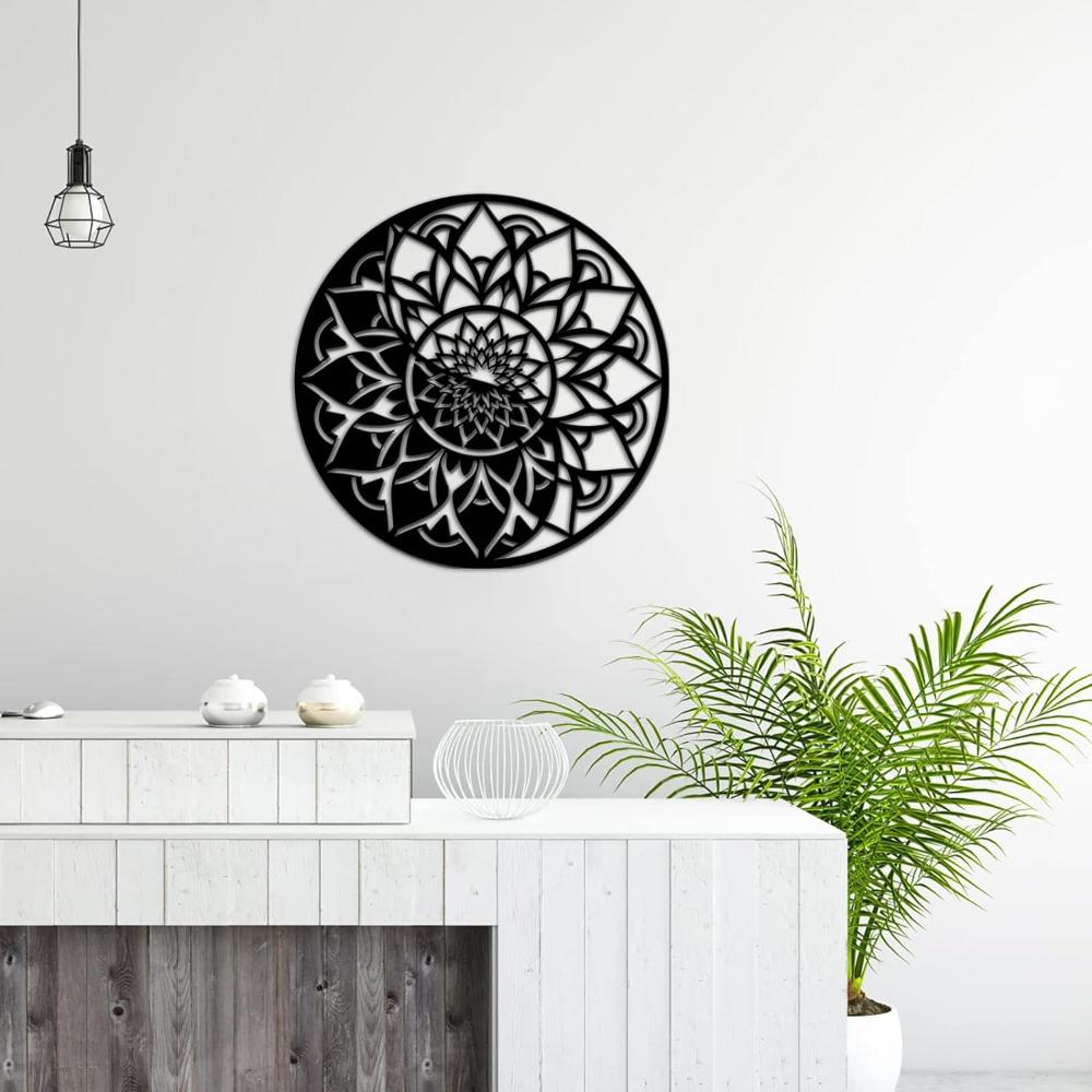  round black metal wall art with an intricate floral mandala design, displayed in a minimalist white room with a green potted plant on the side and decorative ceramic bowls on a modern console table.