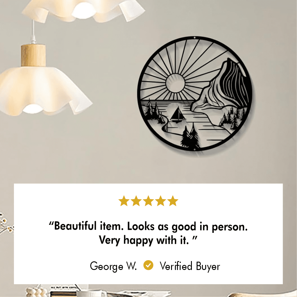 Round metal wall art featuring a scenic design with a sunset, mountain, trees, and a sailboat, mounted on a beige wall beside modern pendant lights. A customer review below reads, "Beautiful item. Looks as good in person. Very happy with it," rated 5 stars by George W., a verified buyer.