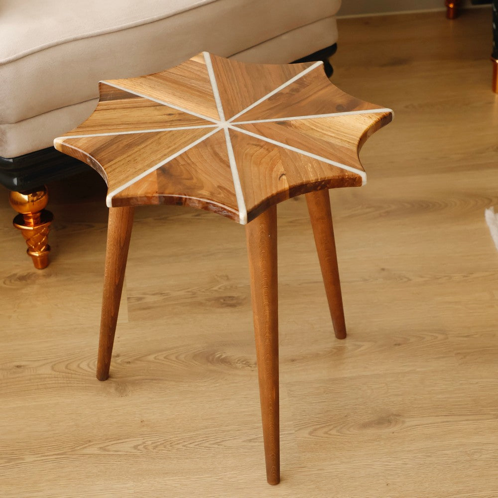 Star-shaped wooden side table with a geometric design featuring white inlay patterns, placed on a wooden floor in a cozy living room setting.