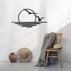 Minimalist metal wall art of a sunset over water with two birds flying, displayed in a cozy corner with a wooden chair, beige throw blanket, a hat, and rustic decor elements such as a woven basket and vase