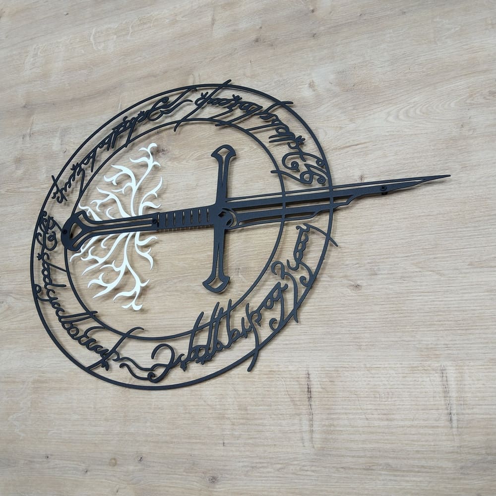 A detailed black metal wall art featuring a sword centered within a circular design with intricate inscriptions, set on a wooden floor.