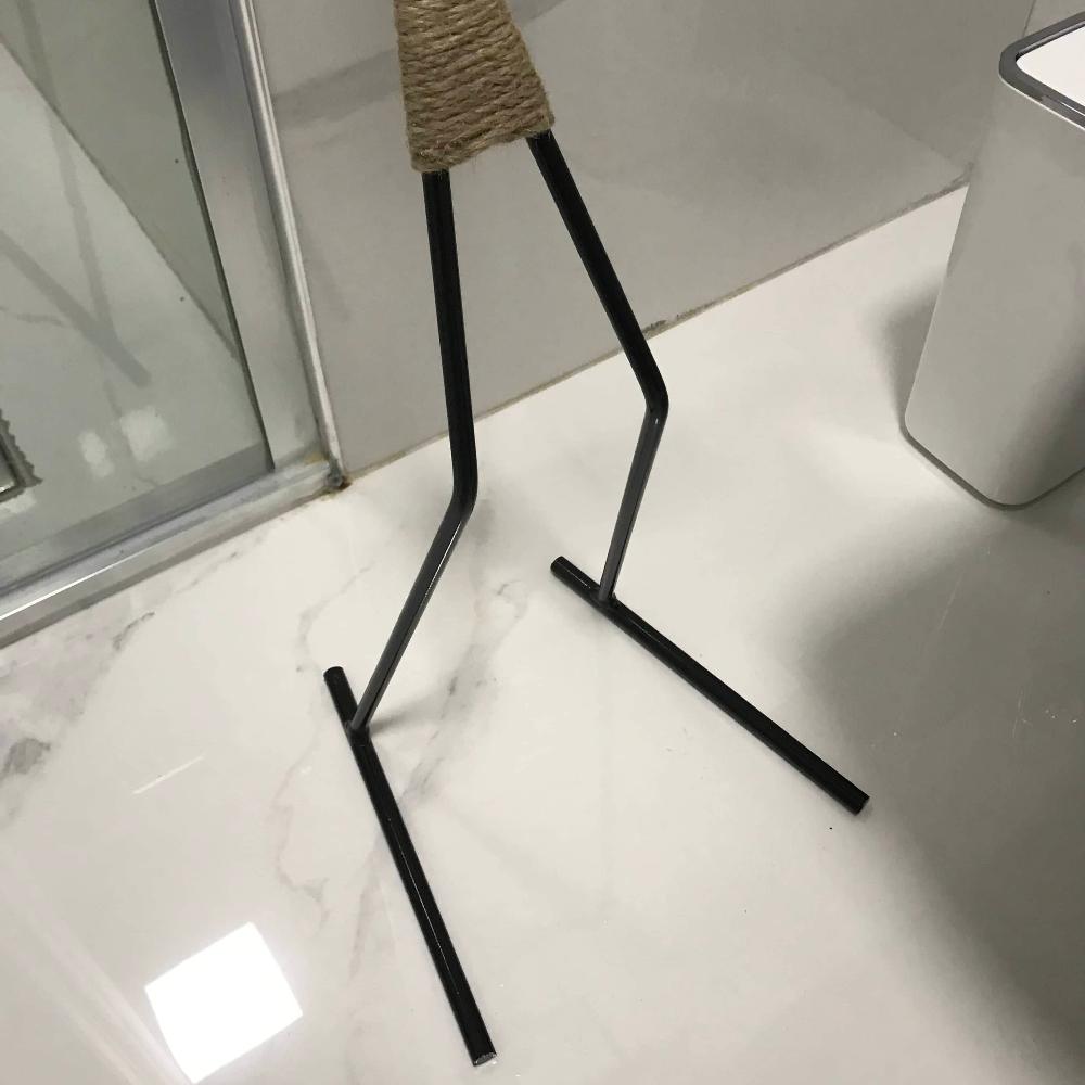 Close-up of the black metal base of a minimalist figure-shaped toilet paper holder, shown on a white marble bathroom floor.