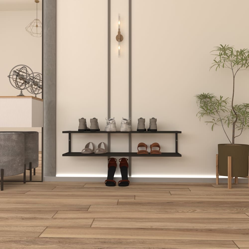 A modern two-tier black metal shoe rack mounted on a light beige wall, displaying various pairs of shoes. The wall features minimalistic vertical lighting, and the floor is a warm wooden design. A small potted plant adds a natural touch to the decor on the right, and part of a stylish living area is visible in the background.