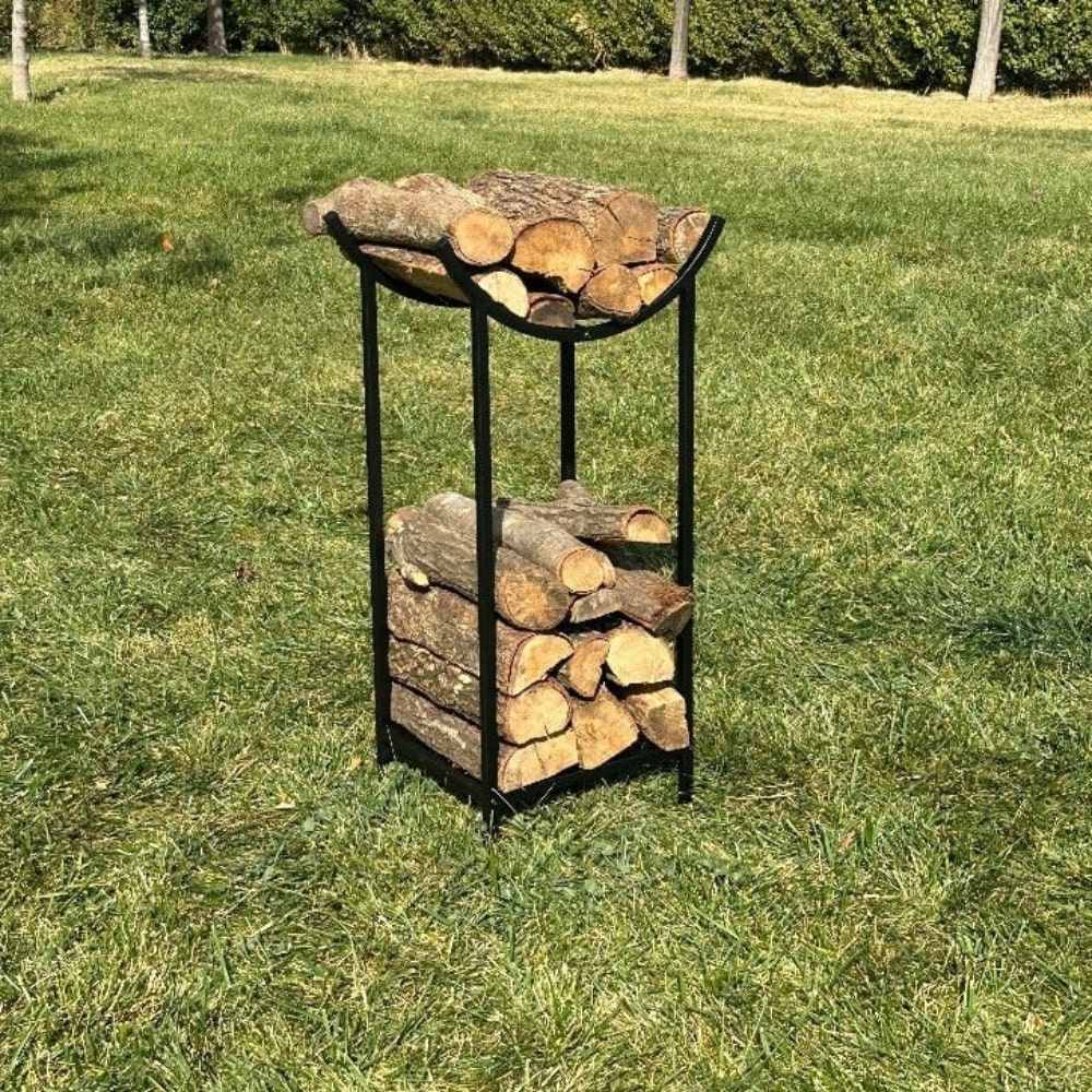 A sleek black metal firewood holder with an arched top section for kindling and a bottom section for logs, displayed on a green lawn for outdoor use