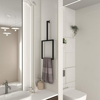 Minimalist black vertical towel rack mounted on a white bathroom wall, holding a folded gray towel, next to a modern sink and mirror with soft lighting and neutral decor.