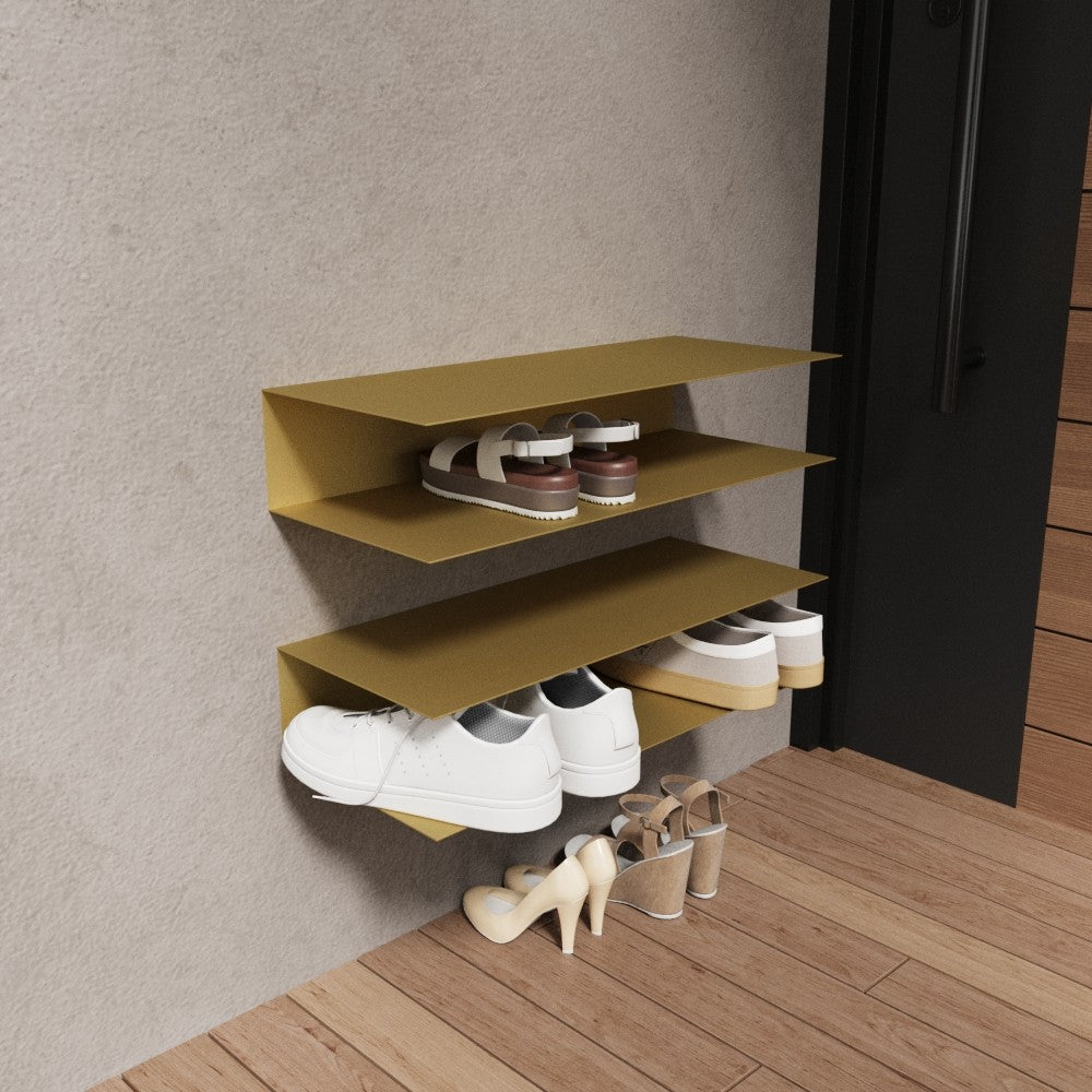 A gold wall-mounted horizontal shoe rack with three shelves, presenting a stylish and unique touch in an entryway with wooden flooring and minimal decor.